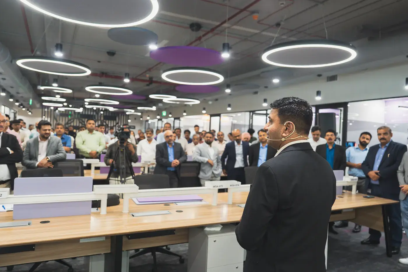 A host presenting to a standing audience across an open-plan office floor